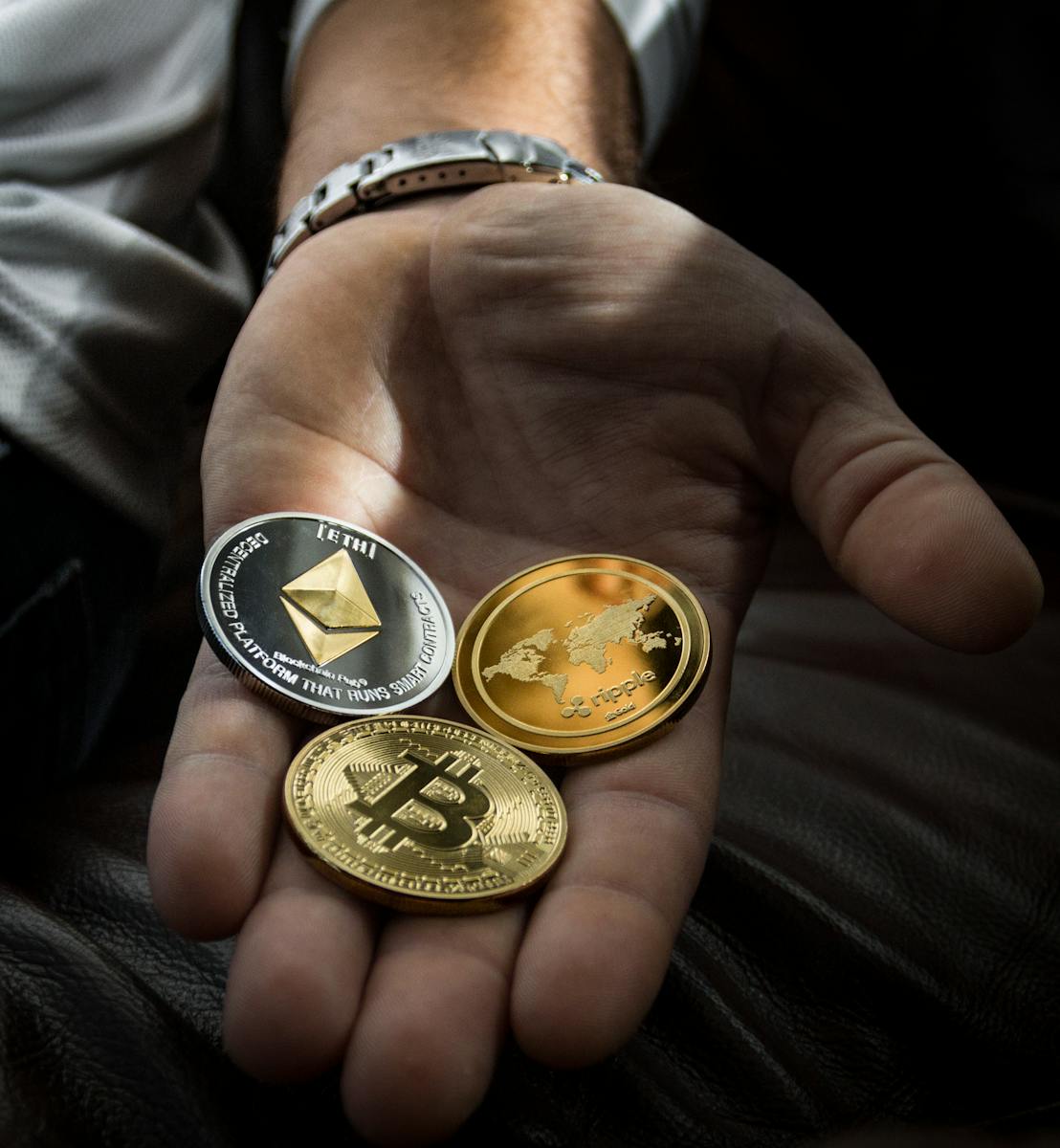 Hand holding Bitcoin, Ethereum, and Ripple coins representing digital currency.