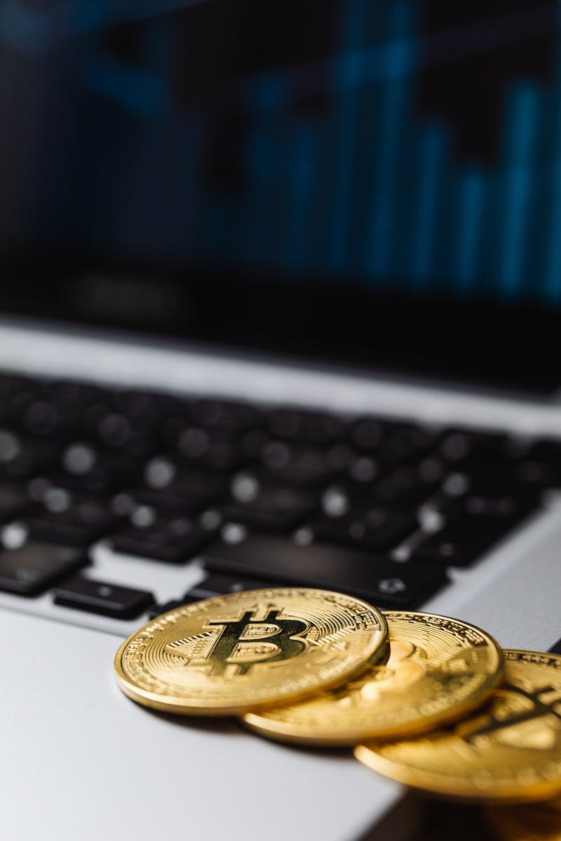 Close-up of gold Bitcoin coins on a laptop keyboard with financial chart in background.